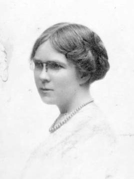 A photograph of Dorothy Richardson. She has centre-parted hair is wearing a string of pearls and a pince-nez with round lenses.